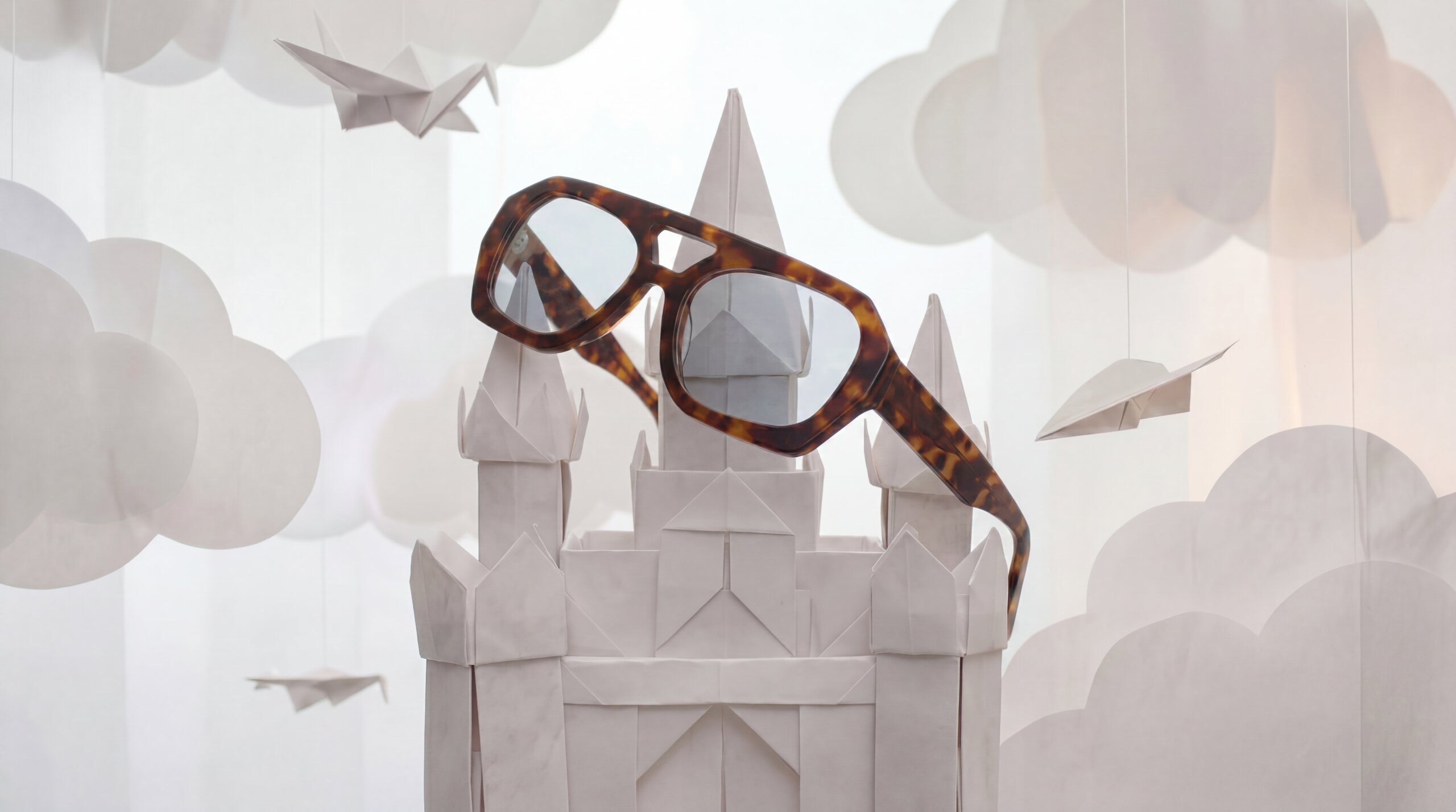 Occhiali da vista su un castello di origami tra nuvole e aeroplanini di carta